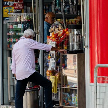 Two men at a street vendor stall exchanging goods in a bustling urban area.