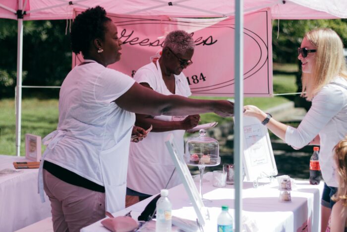 Two women selling goods to a customer at an outdoor stall during the day.